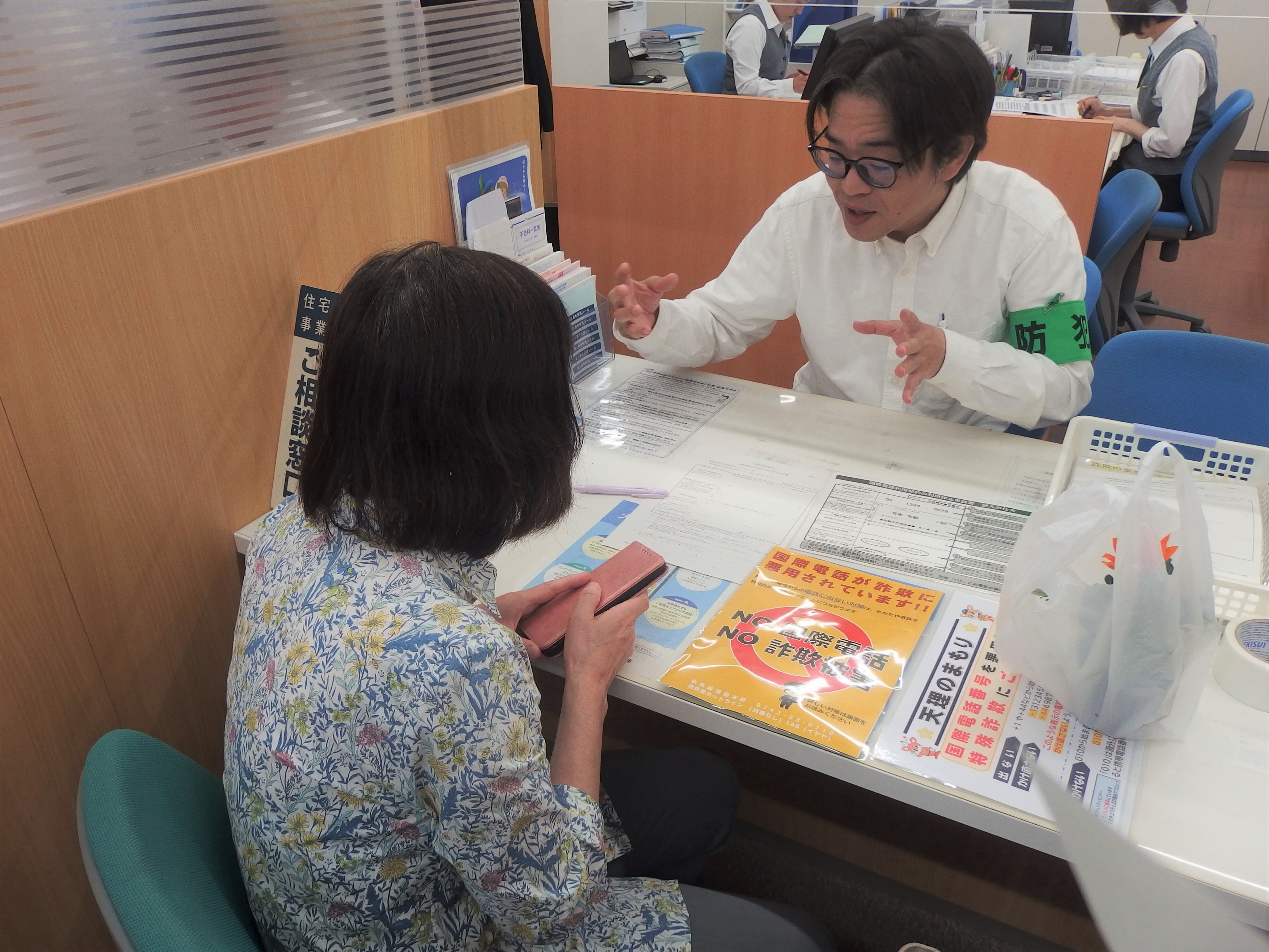 窓口で来客者が詐欺電話の注意喚起チラシの説明を聞いている様子