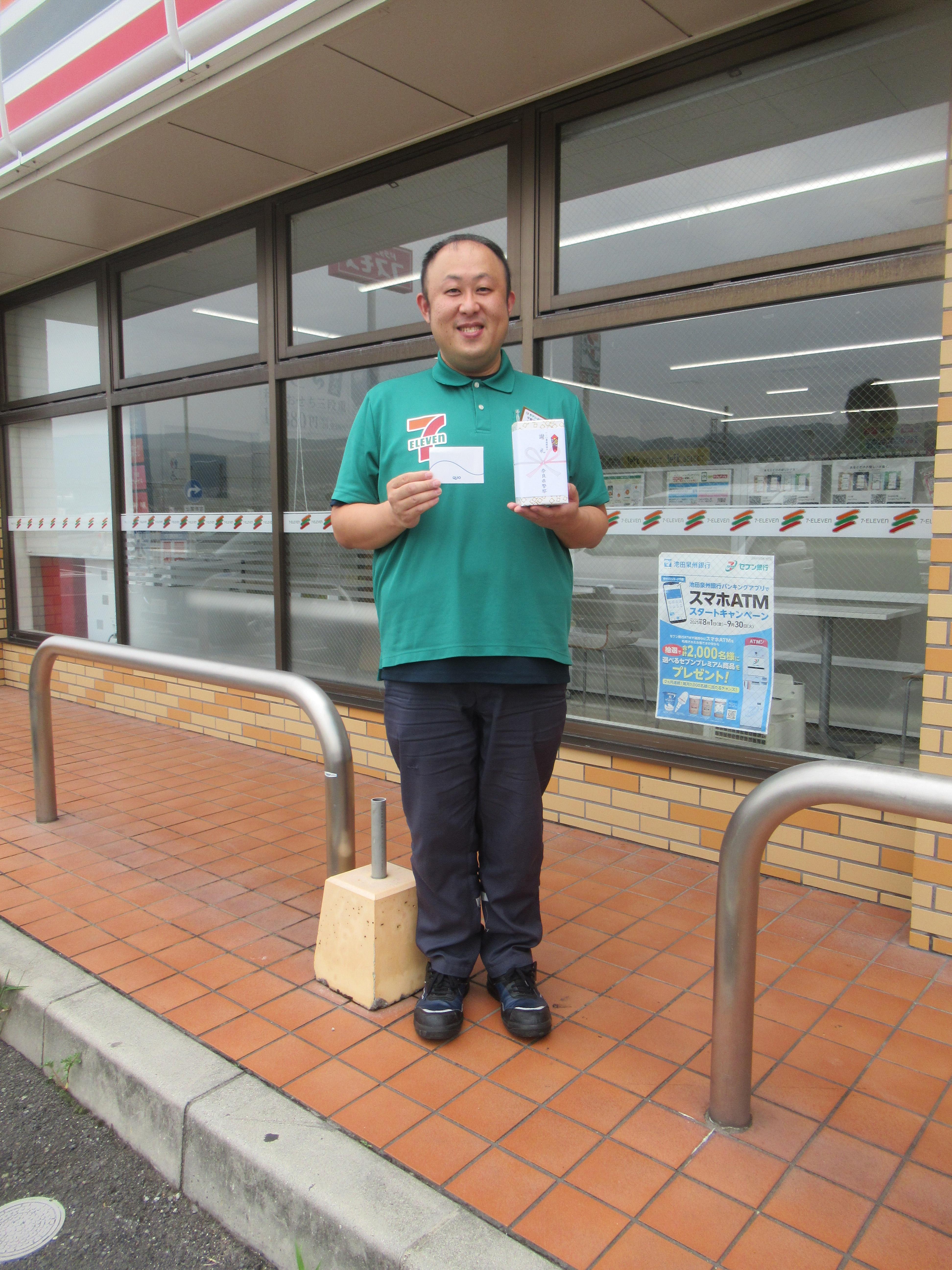 コンビニエンスストア店長が謝礼品を持って立っている様子