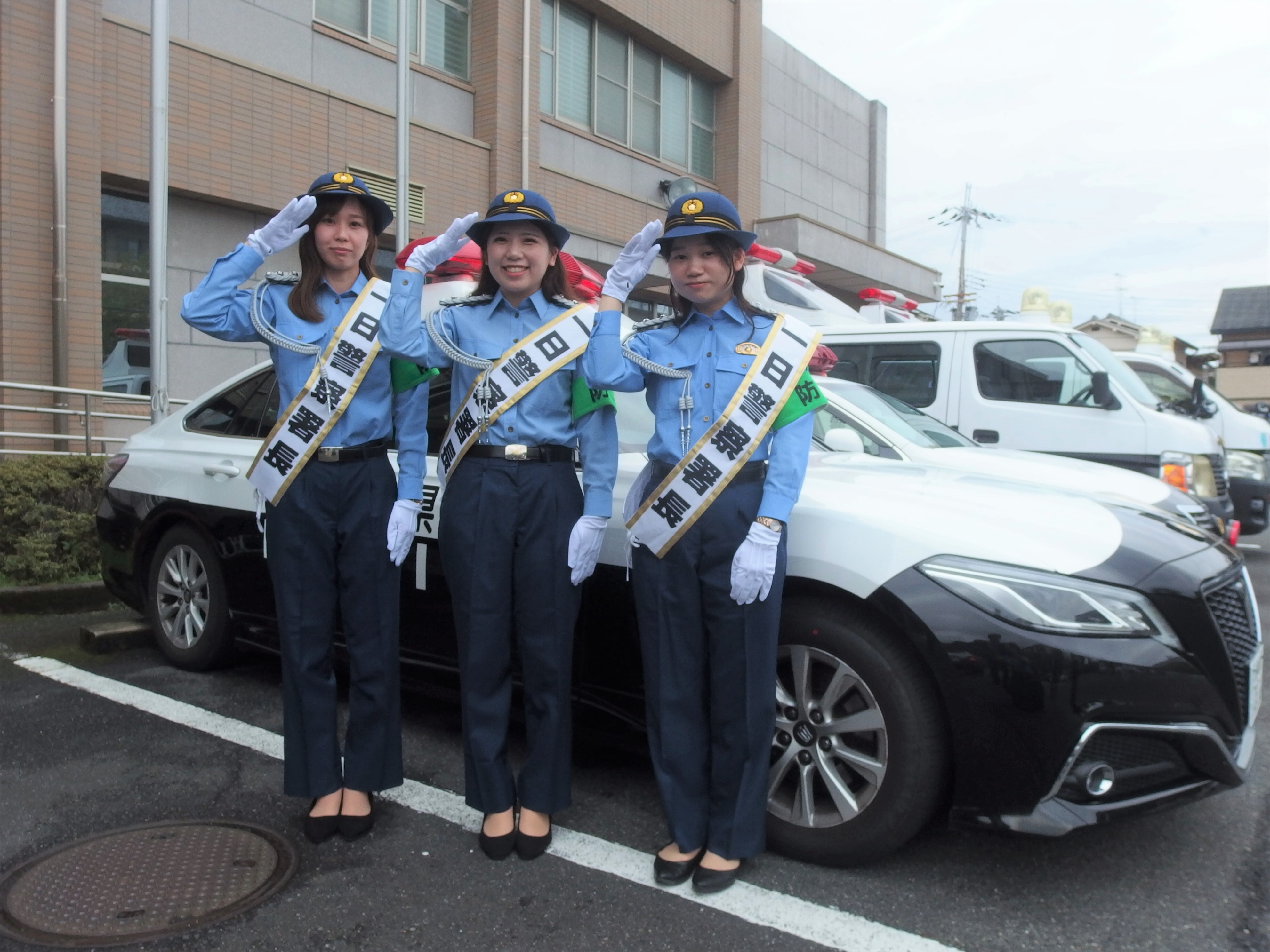 一日警察署長の三人がパトカーの前で立っている様子