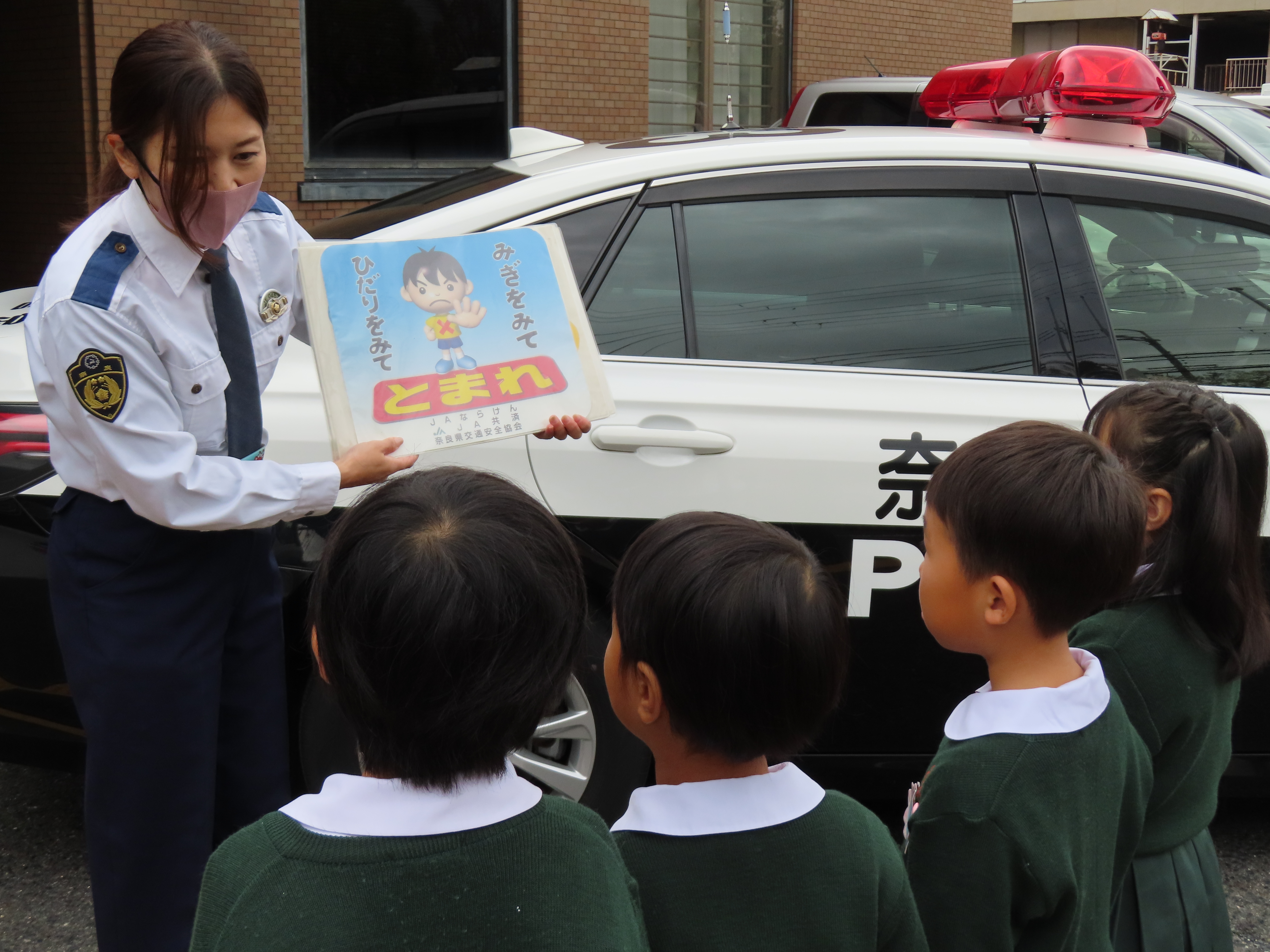 園児達がパトカーの前で警察官のお話を聞いている様子