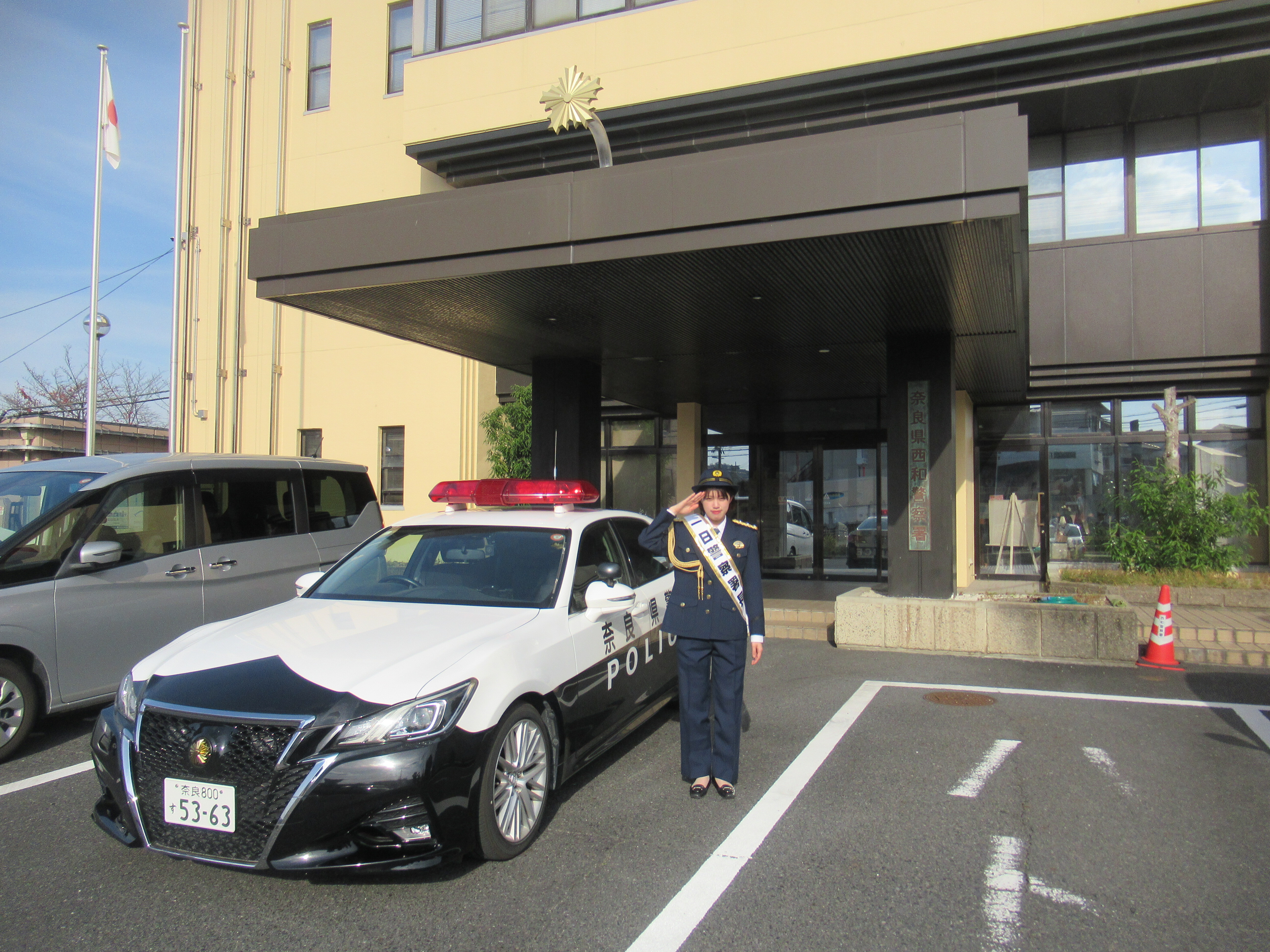 一日署長が警察署前でパトカーと一緒に写っている写真